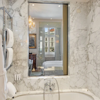 A unique hotel suite design featuring a window that connects a luxurious marble bathroom to the bedroom.
