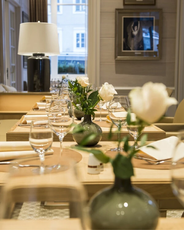 Elegant restaurant table set with a white rose in a vase, wine glasses, cloth napkins, and stylish table decoration