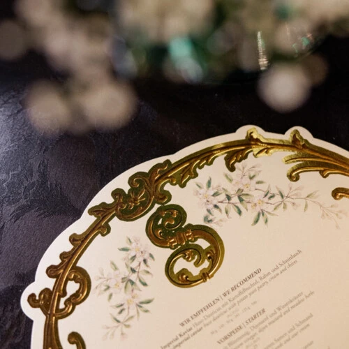 Close-up of a decorative menu card with golden ornaments on the table.