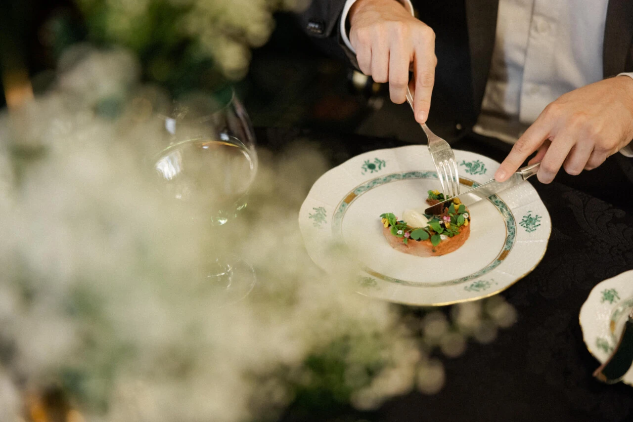 Person cuts into a fine dish on a white porcelain plate with green pattern.
