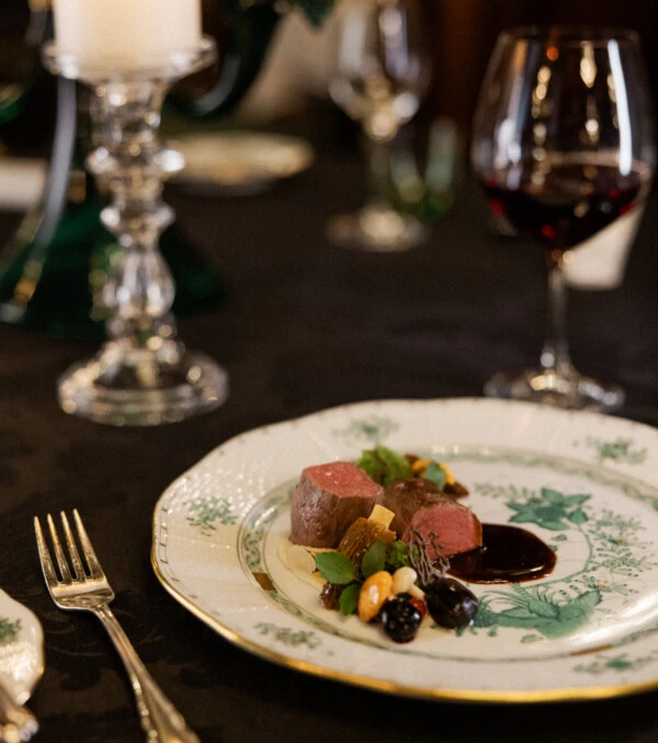 Main course with medium-rare meat, vegetables, and dark sauce on an elegant plate.