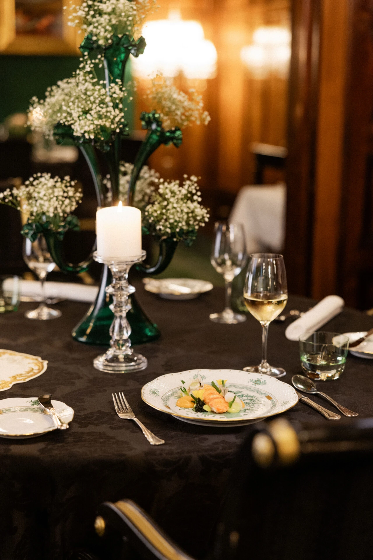 Festively set table with candle, floral arrangement, and plate with fish dish.