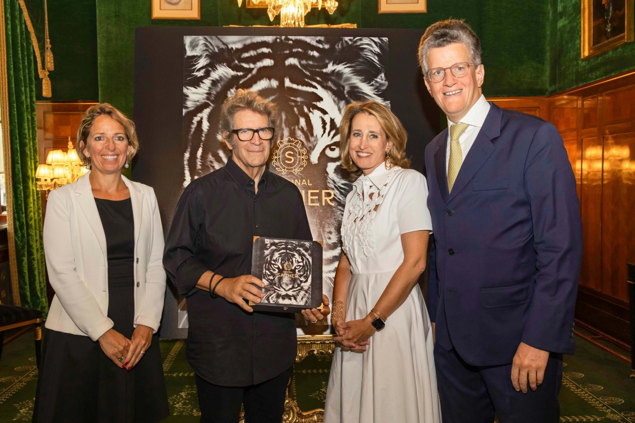 Four people posing indoors with a large tiger portrait backdrop.