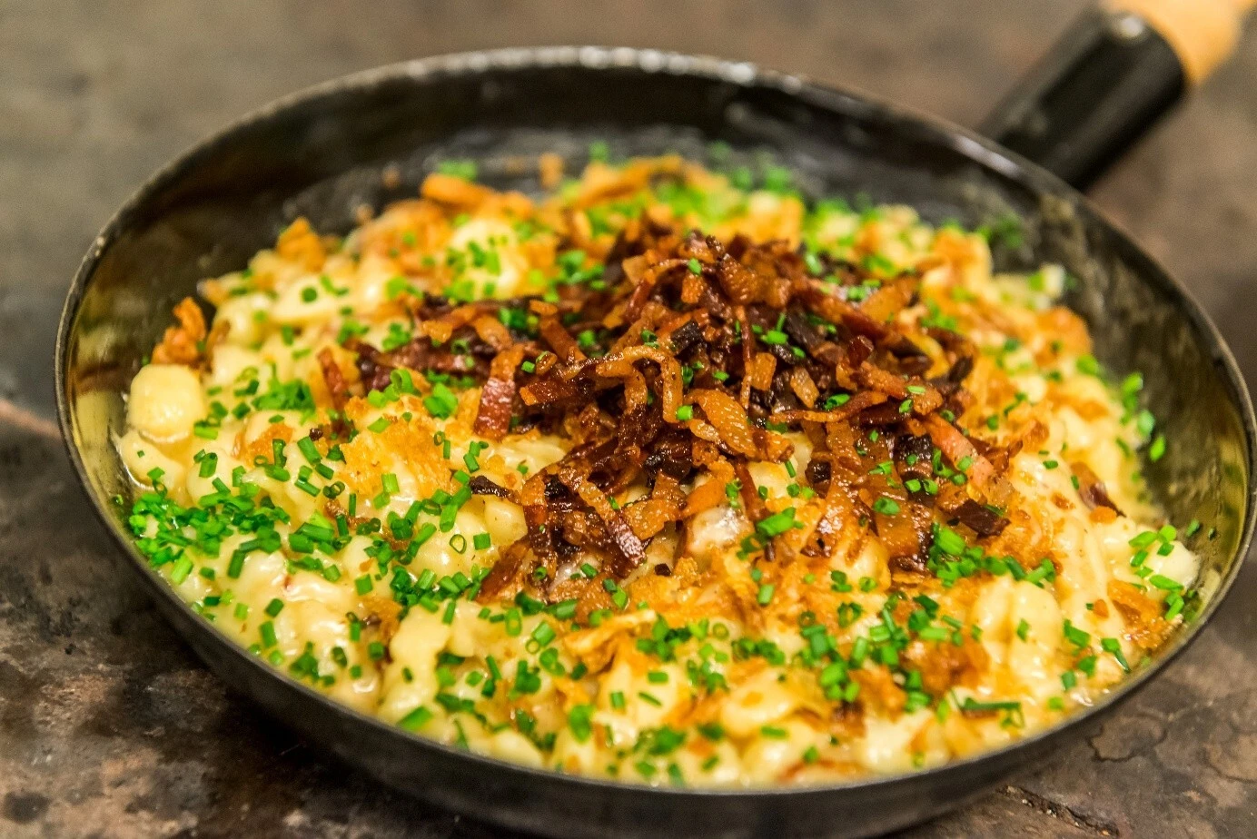 Kasnockn served in a pan with crispy onions and chives – hearty Salzburg specialty made with Alpine cheese.
