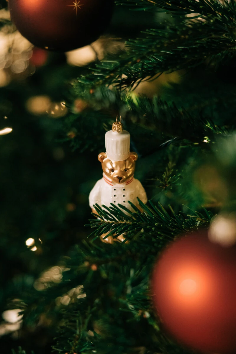 Teddy bear chef Christmas ornament on a green tree with red baubles. Festive holiday decoration.