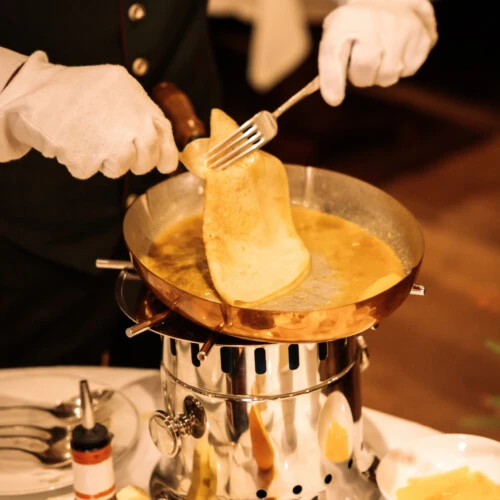 Close-up of a white-gloved server expertly folding a crepe in a copper pan during tableside preparation of Crepes Suzette or Kaiserschmarrn.