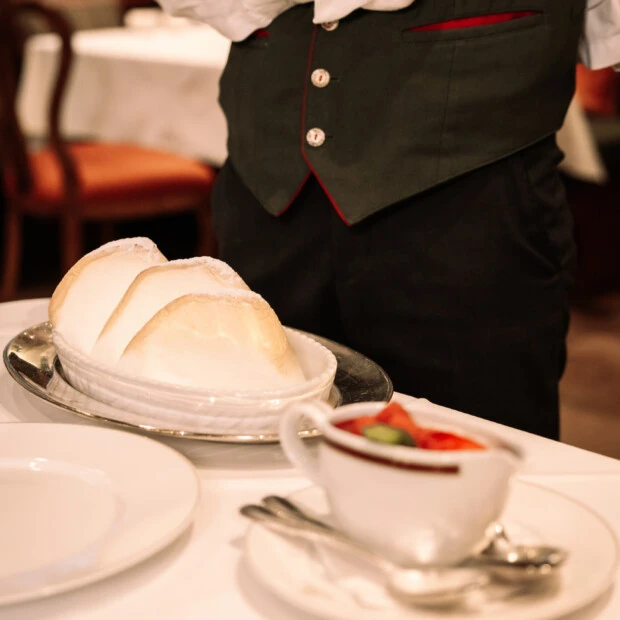 Close-up of fine dining table setting with a waiter in uniform serving Salzburger Nockerl dessert in a luxury hotel restaurant.