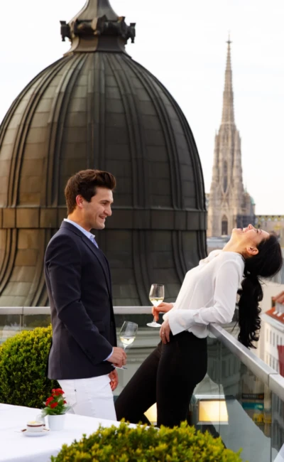 A couple enjoys white wine on a rooftop terrace with a spectacular view of St. Stephen's Cathedral and the Vienna city skyline.