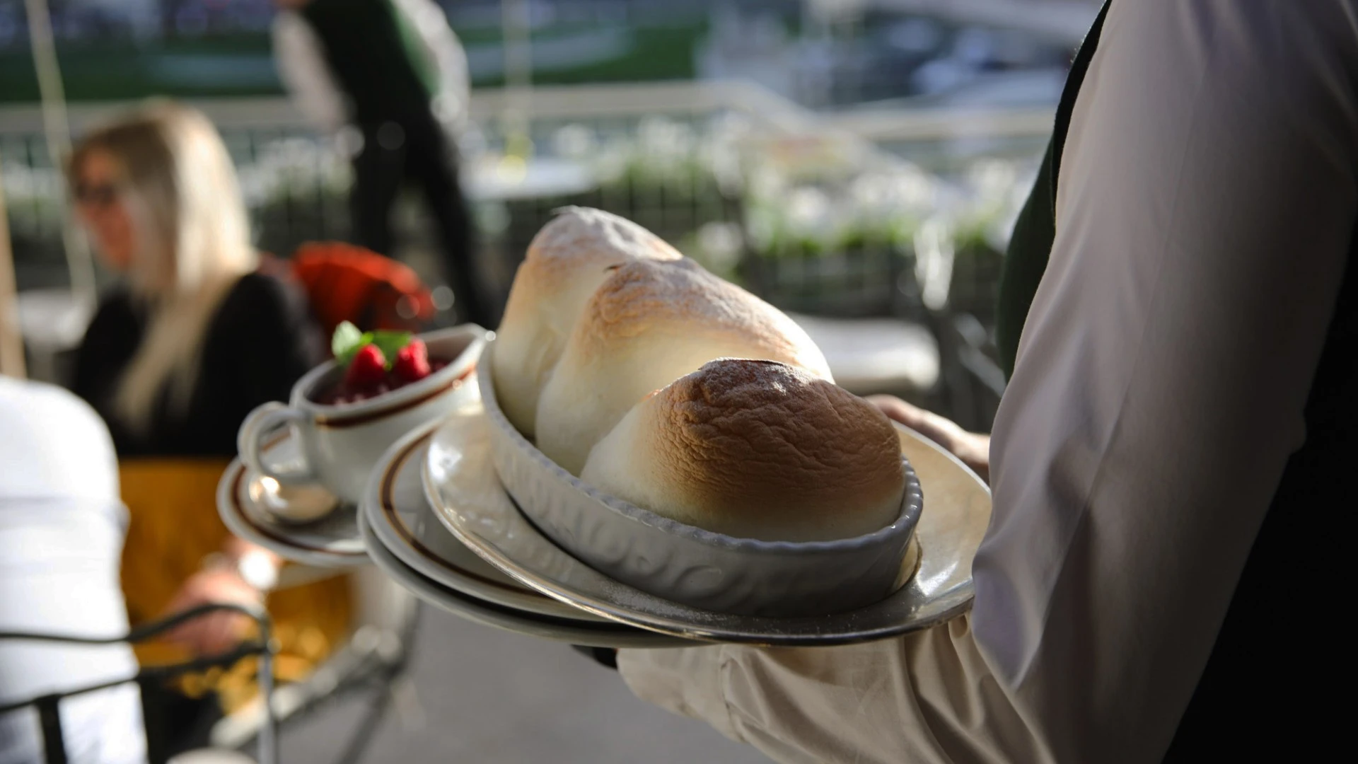 A waiter serves Salzburger Nockerl, a fluffy, golden-baked Austrian dessert, on a sunlit terrace.