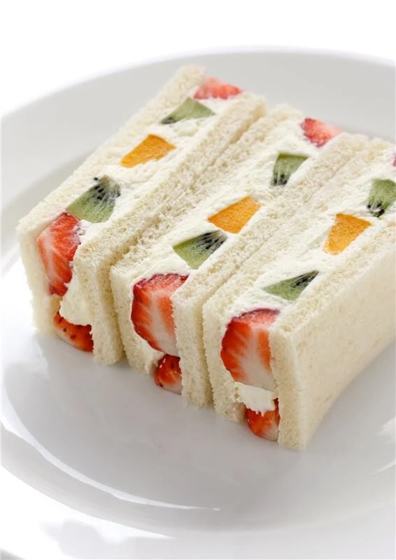 Japanese-style fruit sando with fresh strawberry, kiwi, and mango in whipped cream on white bread.
