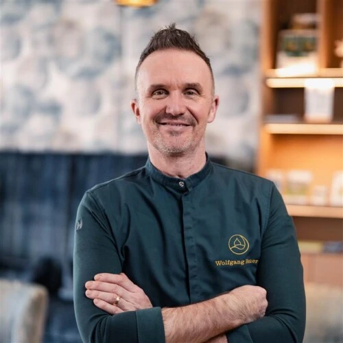 Portrait of a chef at Hotel Sacher, confident posture, modern chef’s jacket and a warm, refined interior setting