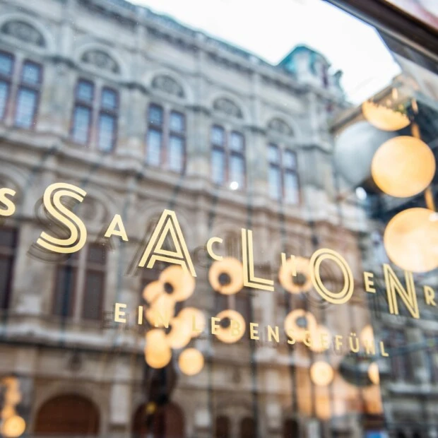 Salon Sacher Wien window signage with reflections of Vienna State Opera building and warm interior lights.