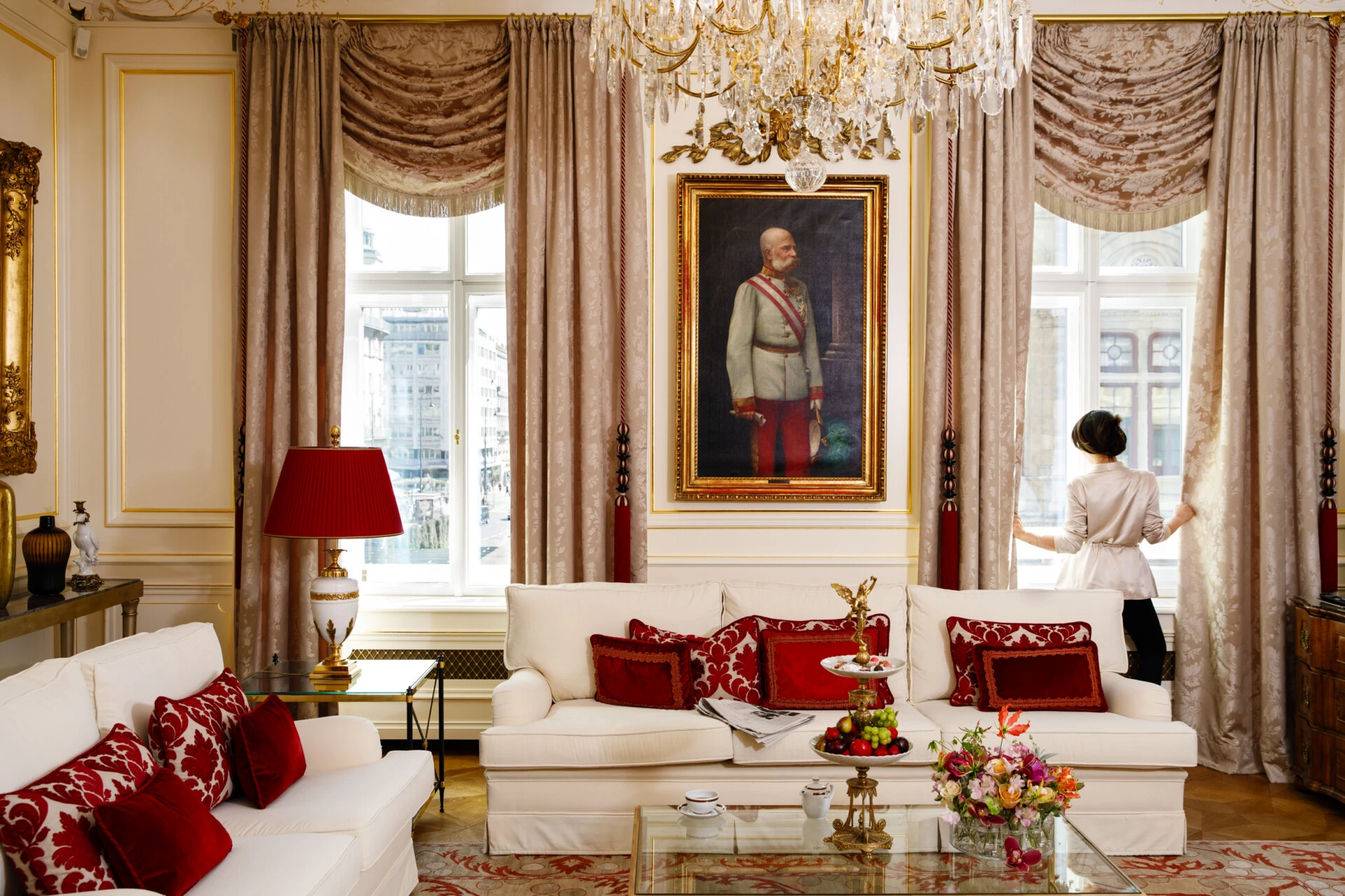 Luxurious suite living room at Hotel Sacher Vienna with white sofas, red décor, chandelier, historic portrait and classic Viennese interior.