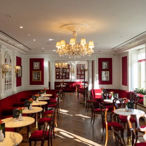 Elegant café at Hotel Sacher Salzburg with red velvet seating, marble tables and chandelier