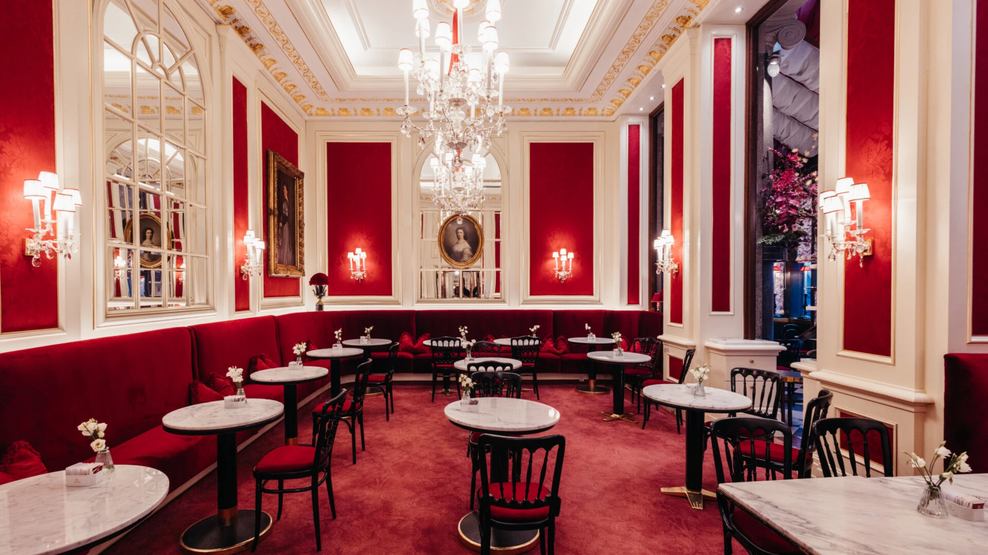 Elegant Café Sacher Vienna with red velvet seating, marble tables, chandeliers and classic wall décor