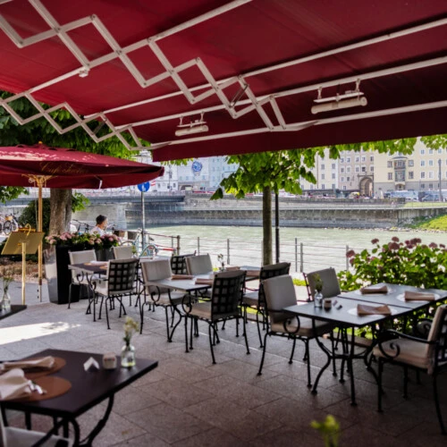 Café Sacher Salzburg terrace by the Salzach river with covered seating and views of the old town