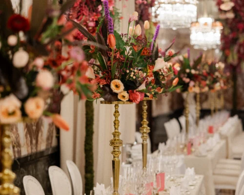 Elegantly set banquet table with tall floral arrangements and crystal chandeliers in the festively decorated Marble Hall at Hotel Sacher