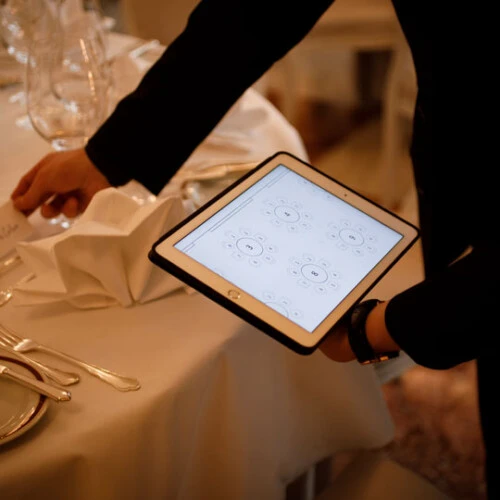 Event staff member using a tablet for digital seating arrangement planning while preparing an elegantly set banquet table
