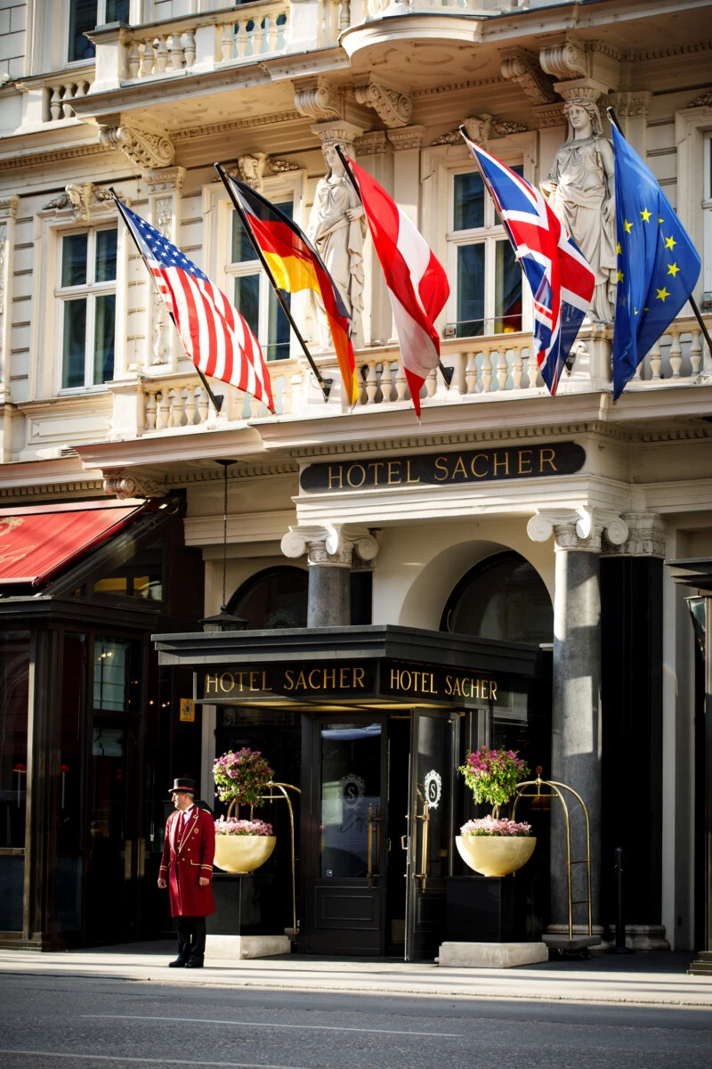 Entrance of Hotel Sacher Vienna with international flags, floral displays and a uniformed doorman
