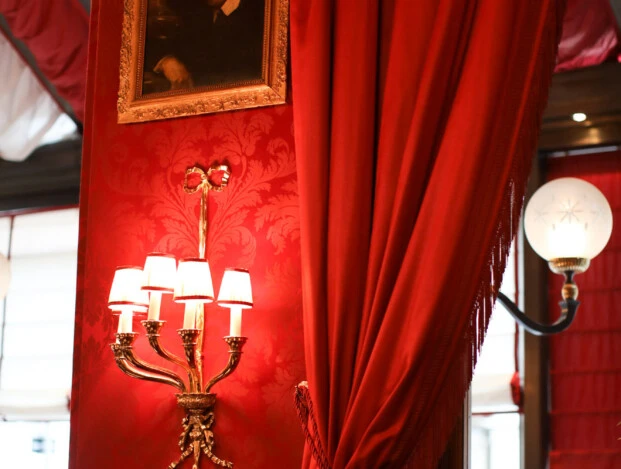 A richly decorated corner of the Rote Bar at Hotel Sacher, featuring opulent red drapes, classic wall sconces, and a framed portrait against patterned red wallpaper.