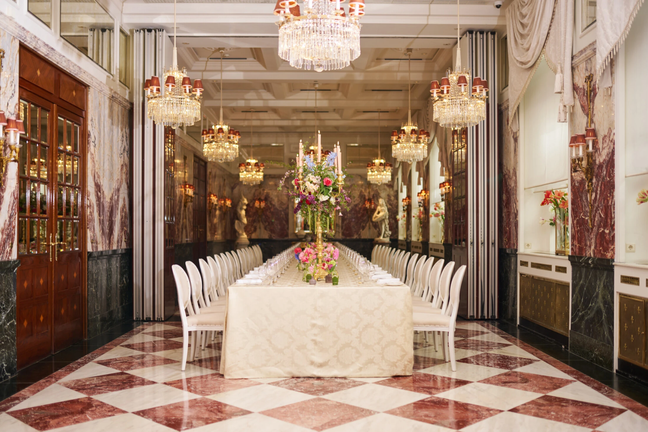 Elegant banquet setup at Hotel Sacher Vienna with long dining table, floral centerpiece, chandeliers and marble interior for weddings and luxury events.