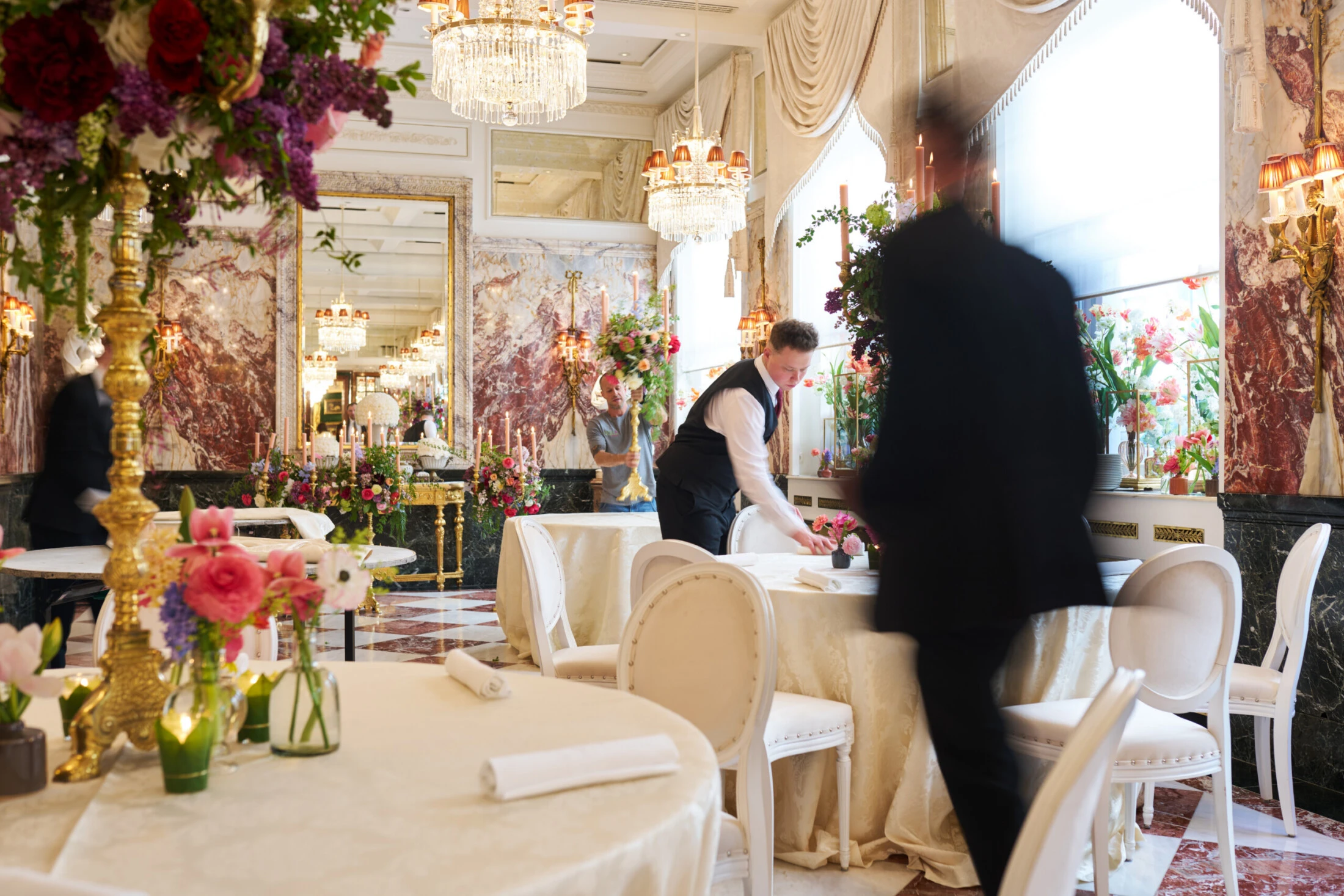 Hotel Sacher Vienna service team setting elegant round tables with floral arrangements, candlelight and chandelier décor for a luxury event.