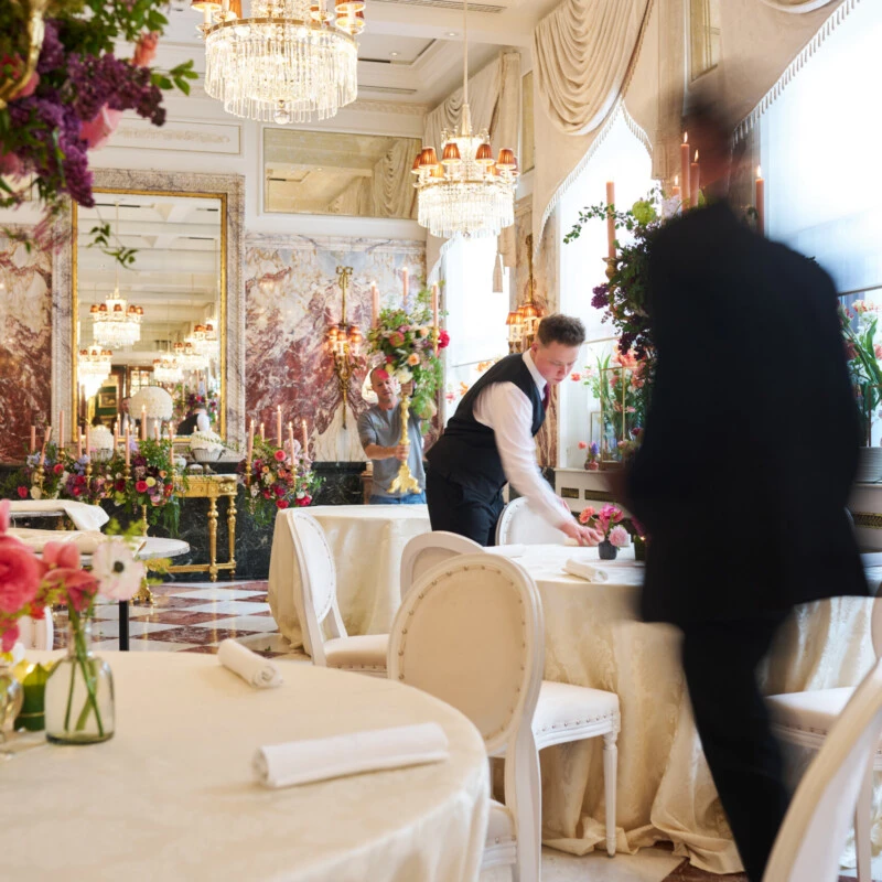 Hotel Sacher Vienna service team setting elegant round tables with floral arrangements, candlelight and chandelier décor for a luxury event.
