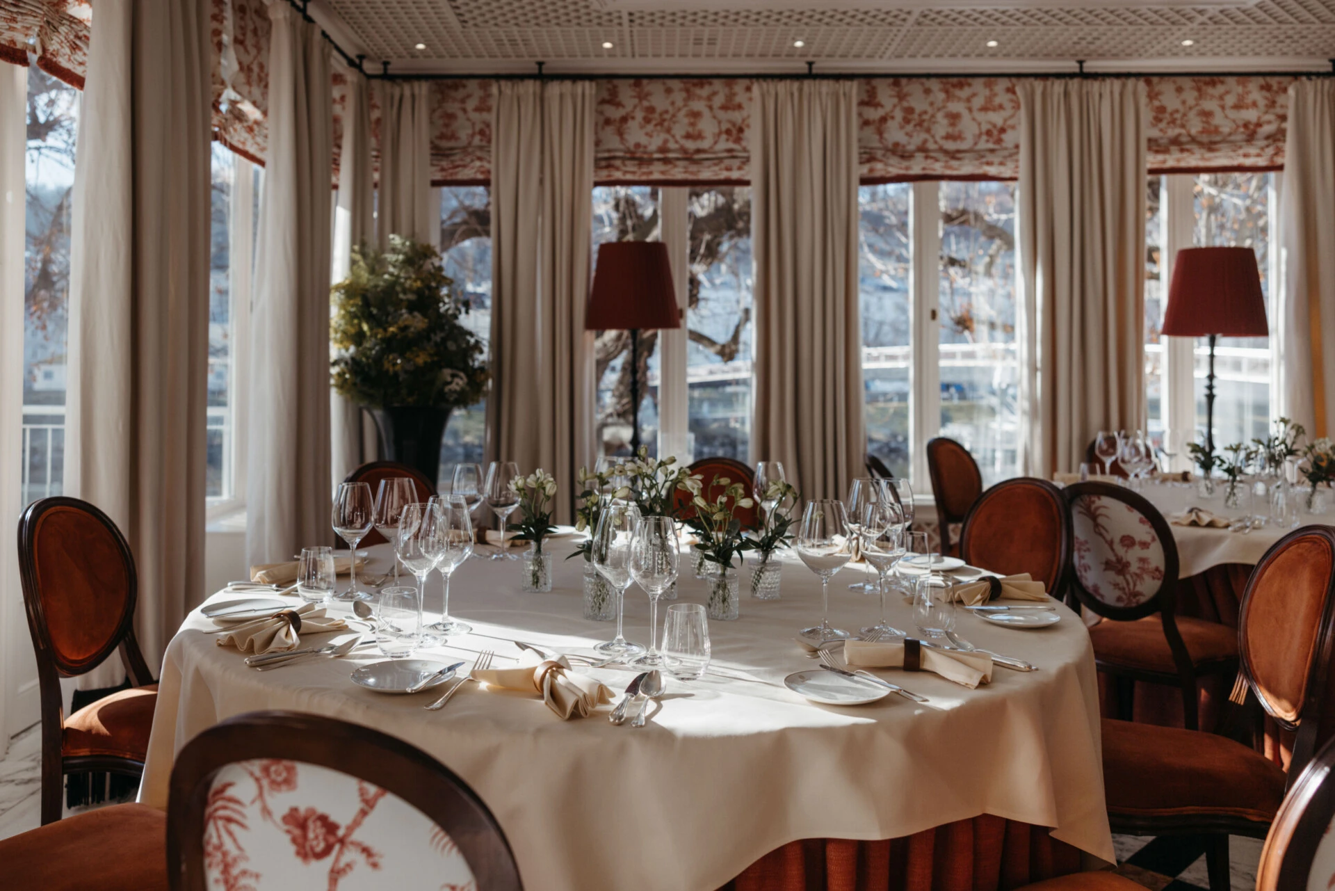 Elegant private dining room at Hotel Sacher Salzburg with round banquet tables, floral centerpieces, fine table settings and views of the Salzach.