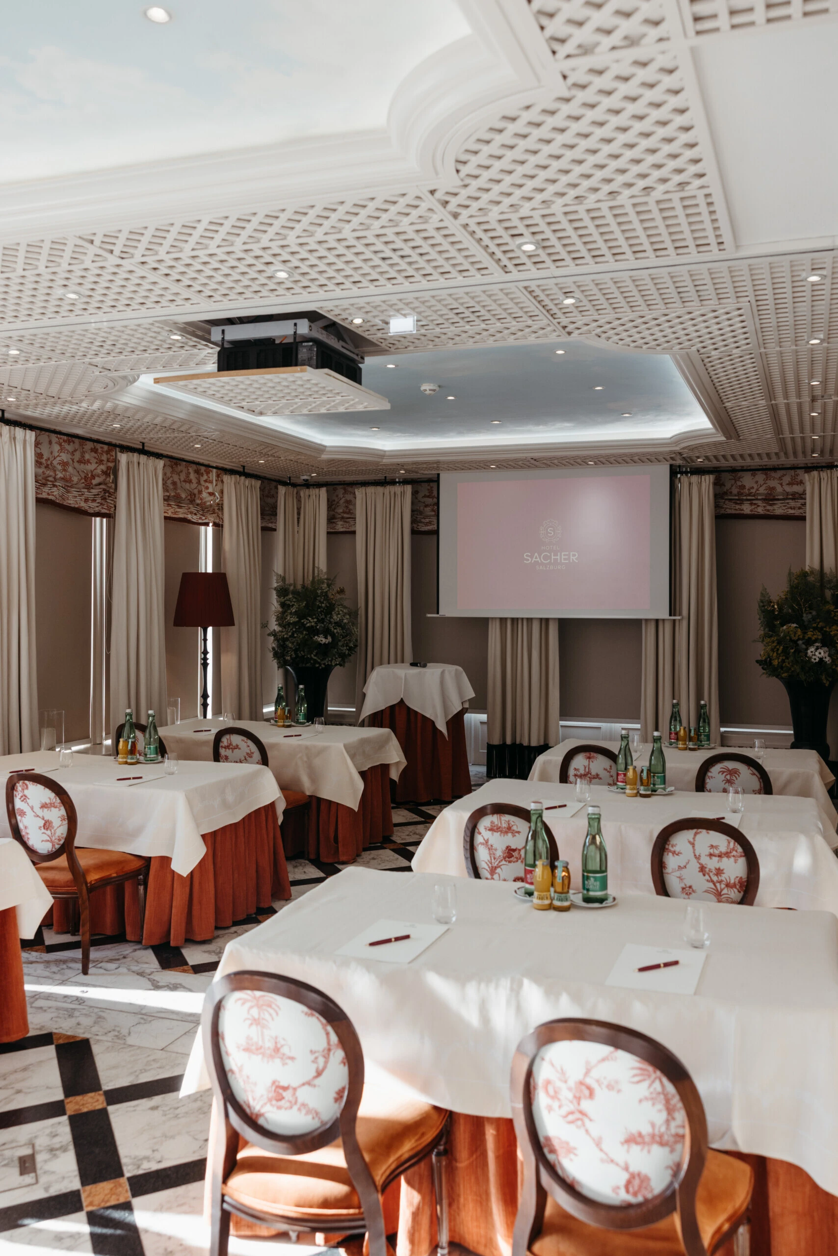 Elegant meeting room at Hotel Sacher Salzburg with banquet tables, projector screen, natural daylight and classic interior design for conferences and private events.
