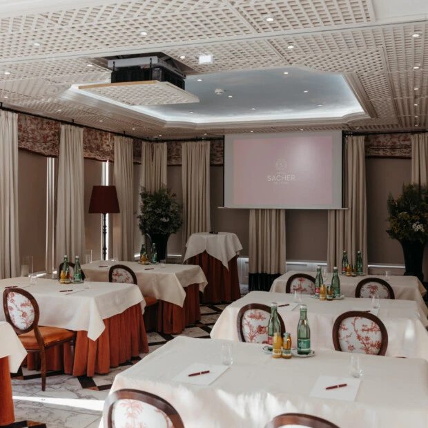 Elegant meeting room at Hotel Sacher Salzburg with banquet tables, projector screen, natural daylight and classic interior design for conferences and private events.