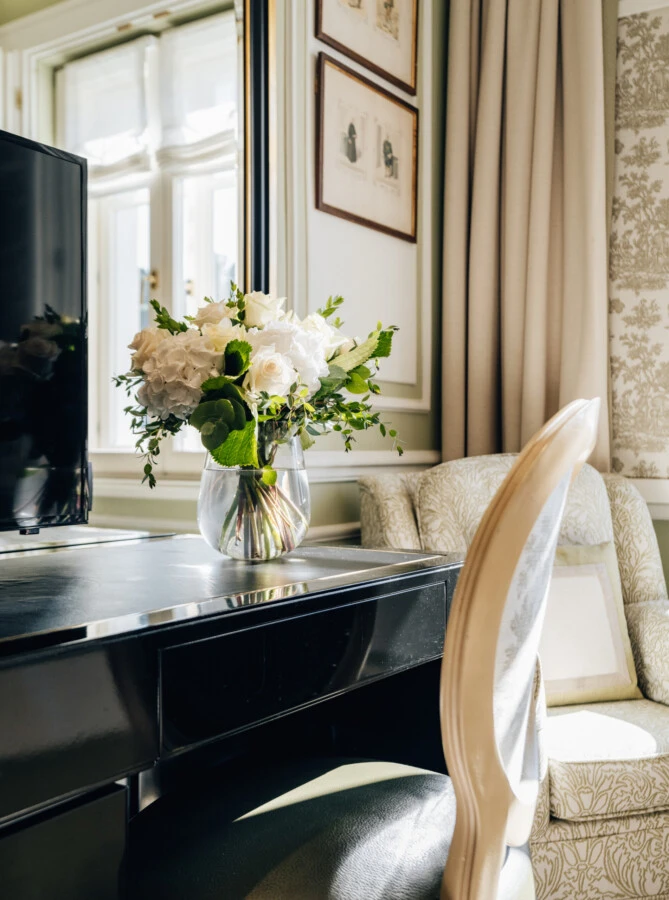 Writing desk in the Deluxe Room with View at Hotel Sacher Salzburg, featuring a white floral arrangement, TV and classic armchair