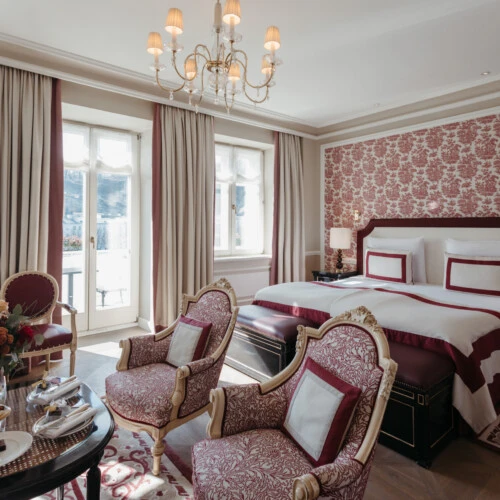 Junior Suite with View at Hotel Sacher Salzburg, featuring an elegant double bed, classic armchairs, red patterned details and large windows