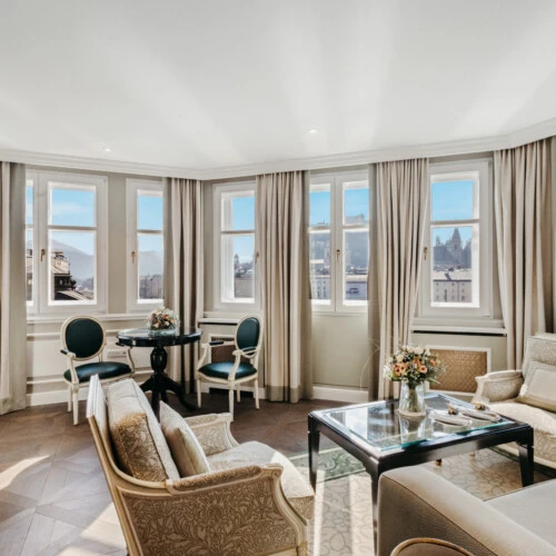Bright living area of the Signature Suite with View at Hotel Sacher Salzburg, featuring classic armchairs, a glass table and panoramic windows