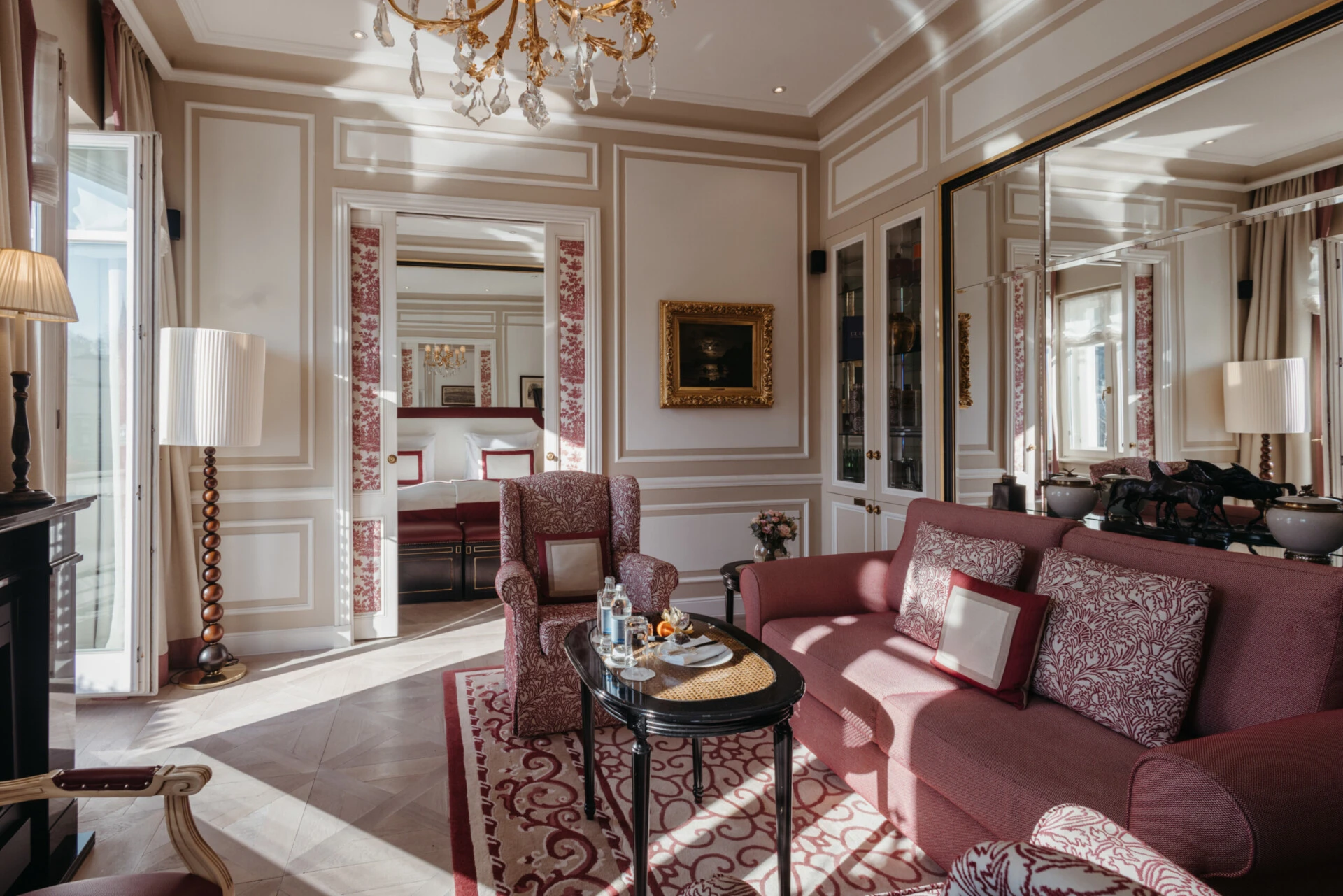 Family suite with a view at the Hotel Sacher in Salzburg, featuring a bedroom, a sitting area, and elegant red patterned accents