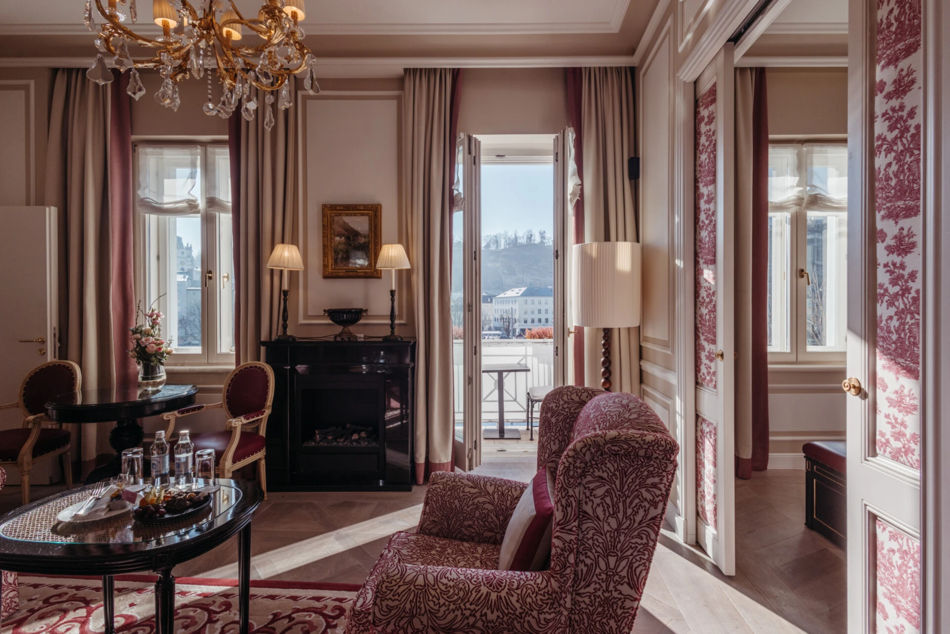 Family suite with a view at the Hotel Sacher in Salzburg, featuring a bedroom, a sitting area, and elegant red patterned accents