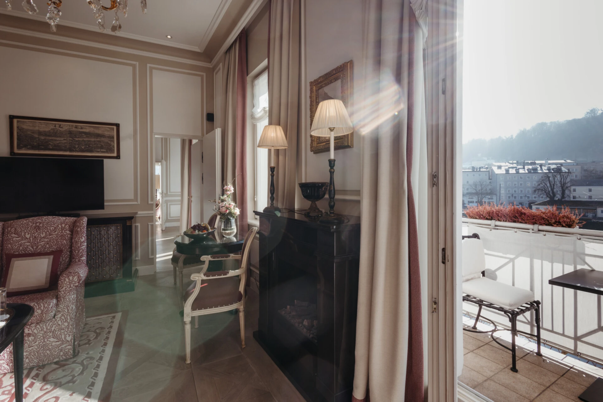 Living area of the Family Suite with a view at the Hotel Sacher Salzburg, featuring a fireplace, dining table, balcony, and a view of the Salzach River