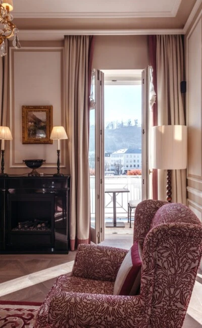 Family suite with a view at the Hotel Sacher in Salzburg, featuring a bedroom, a sitting area, and elegant red patterned accents