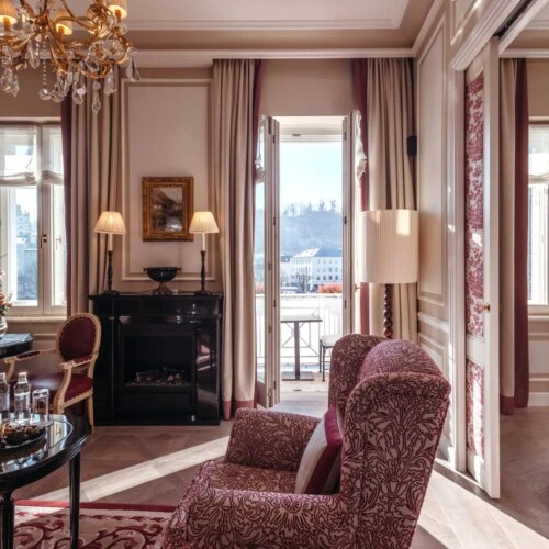 Family suite with a view at the Hotel Sacher in Salzburg, featuring a bedroom, a sitting area, and elegant red patterned accents