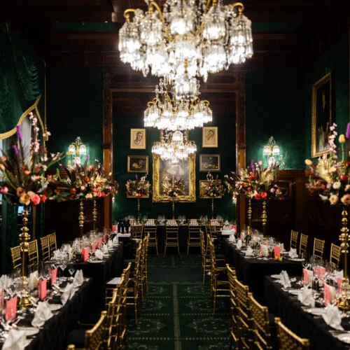 Festively set dining table in the Restaurant Grüne Bar at Hotel Sacher Vienna with tall floral arrangements and gold chairs.
