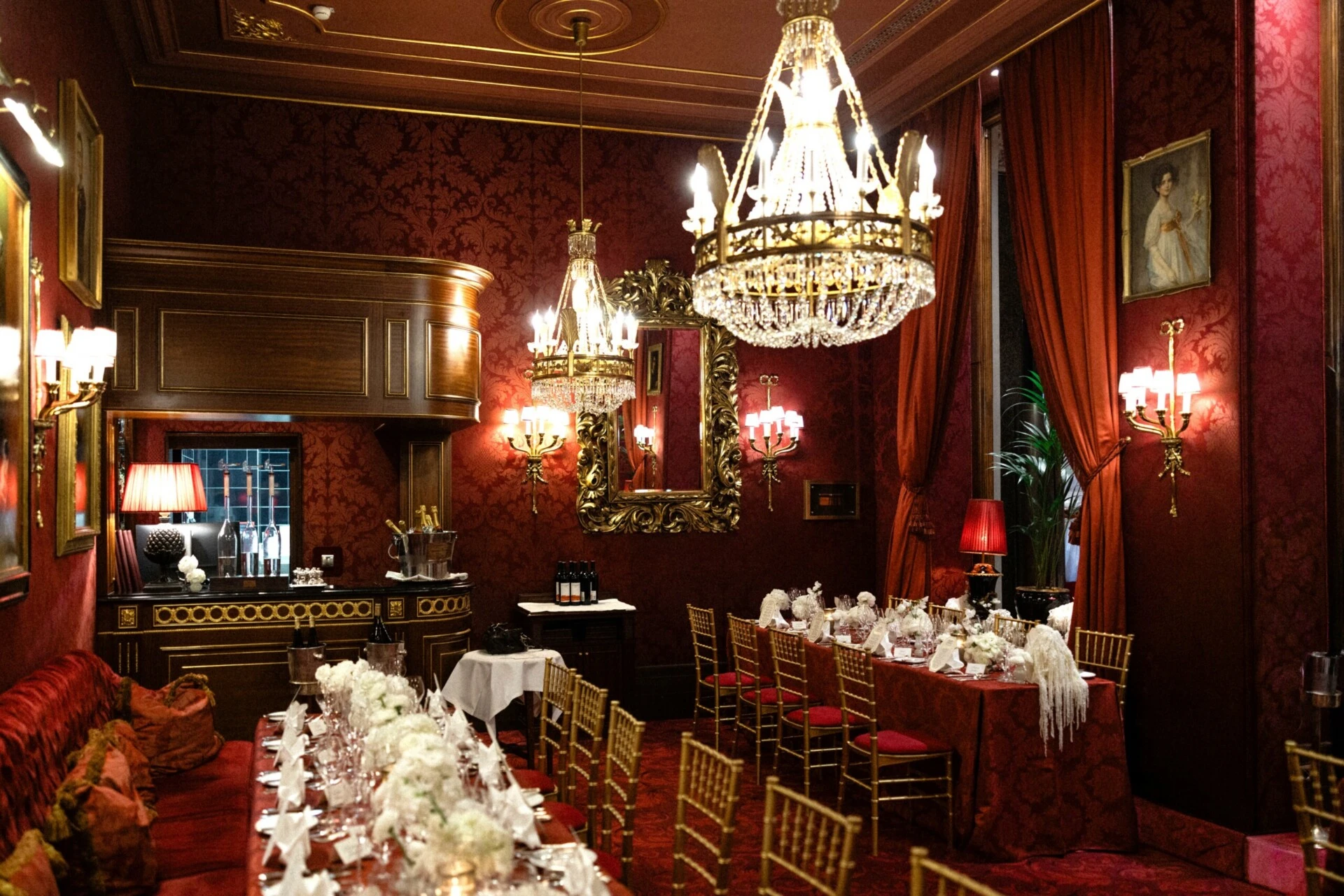 Festively set Restaurant Rote Bar at Hotel Sacher Vienna with crystal chandeliers, red velvet seating, gold chairs and white floral arrangements.