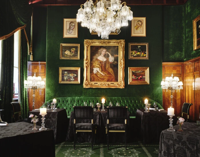 Elegant dining room of the Restaurant Grüne Bar with green velvet walls, a crystal chandelier and historic paintings.
