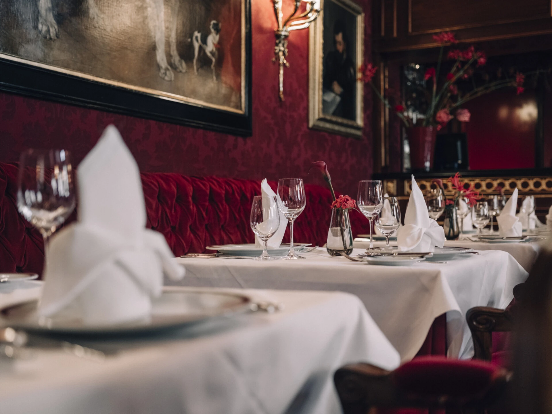 Elegantly set tables in the Restaurant Rote Bar at Hotel Sacher Vienna with red velvet and historic paintings.