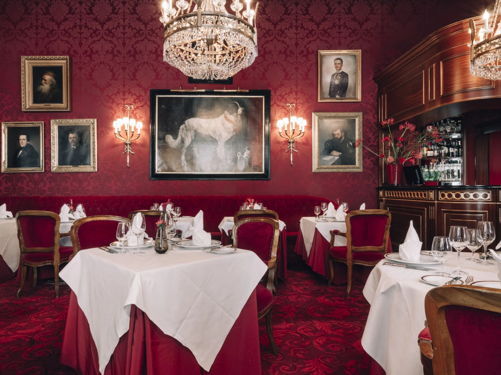 Elegant dining room of the Restaurant Rote Bar at Hotel Sacher Vienna with red velvet chairs, crystal chandeliers and historic paintings.