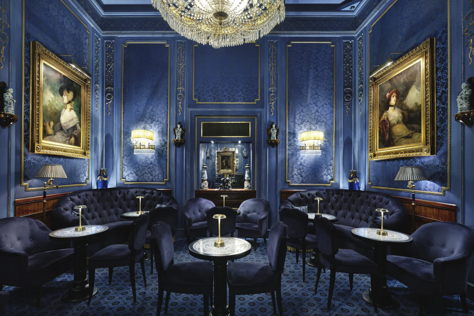 Elegant lounge area of the Blaue Bar with blue velvet seating and historic paintings.