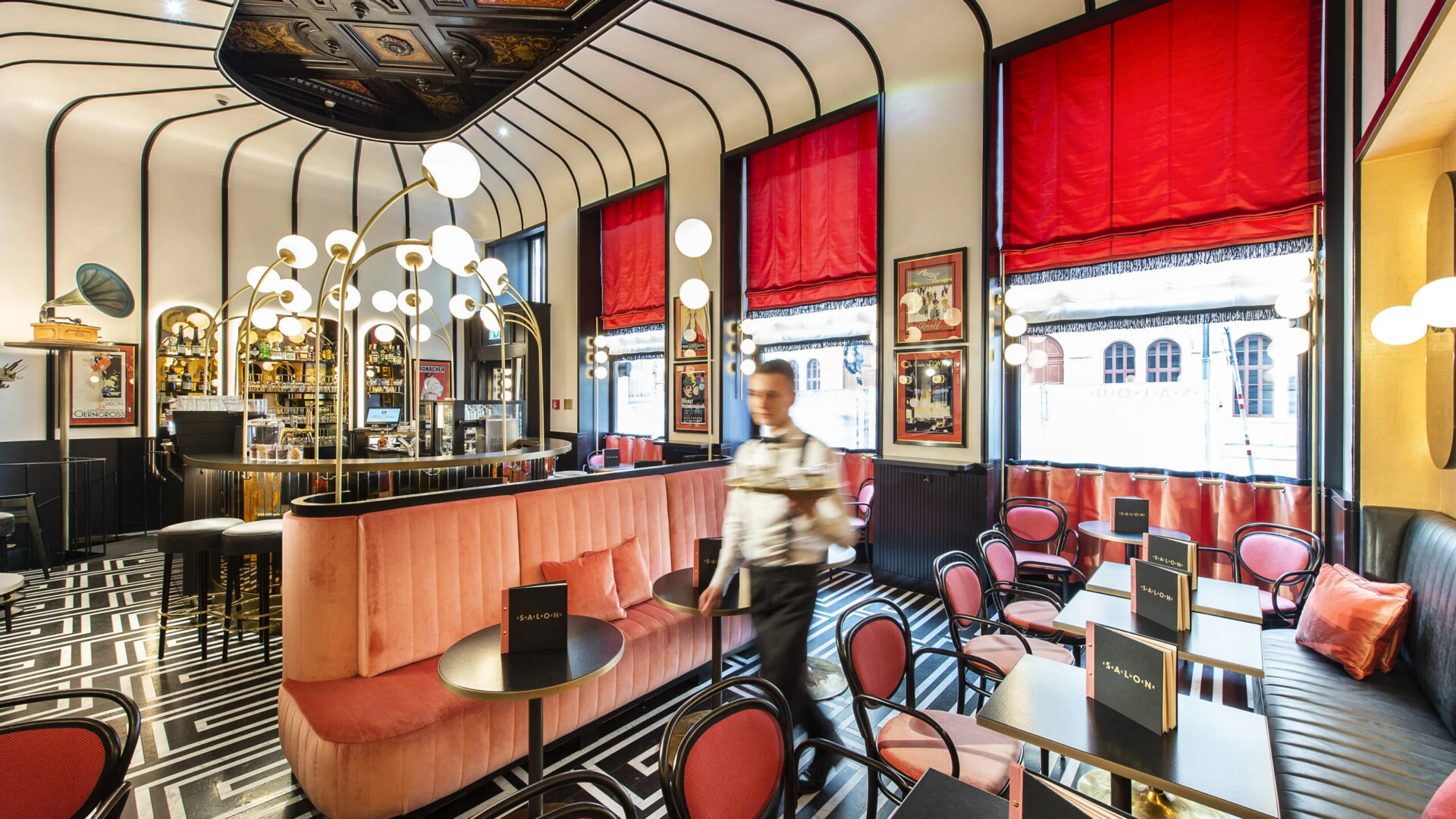 Modern dining area of Salon Sacher with red furnishings, a graphic floor and a member of staff.