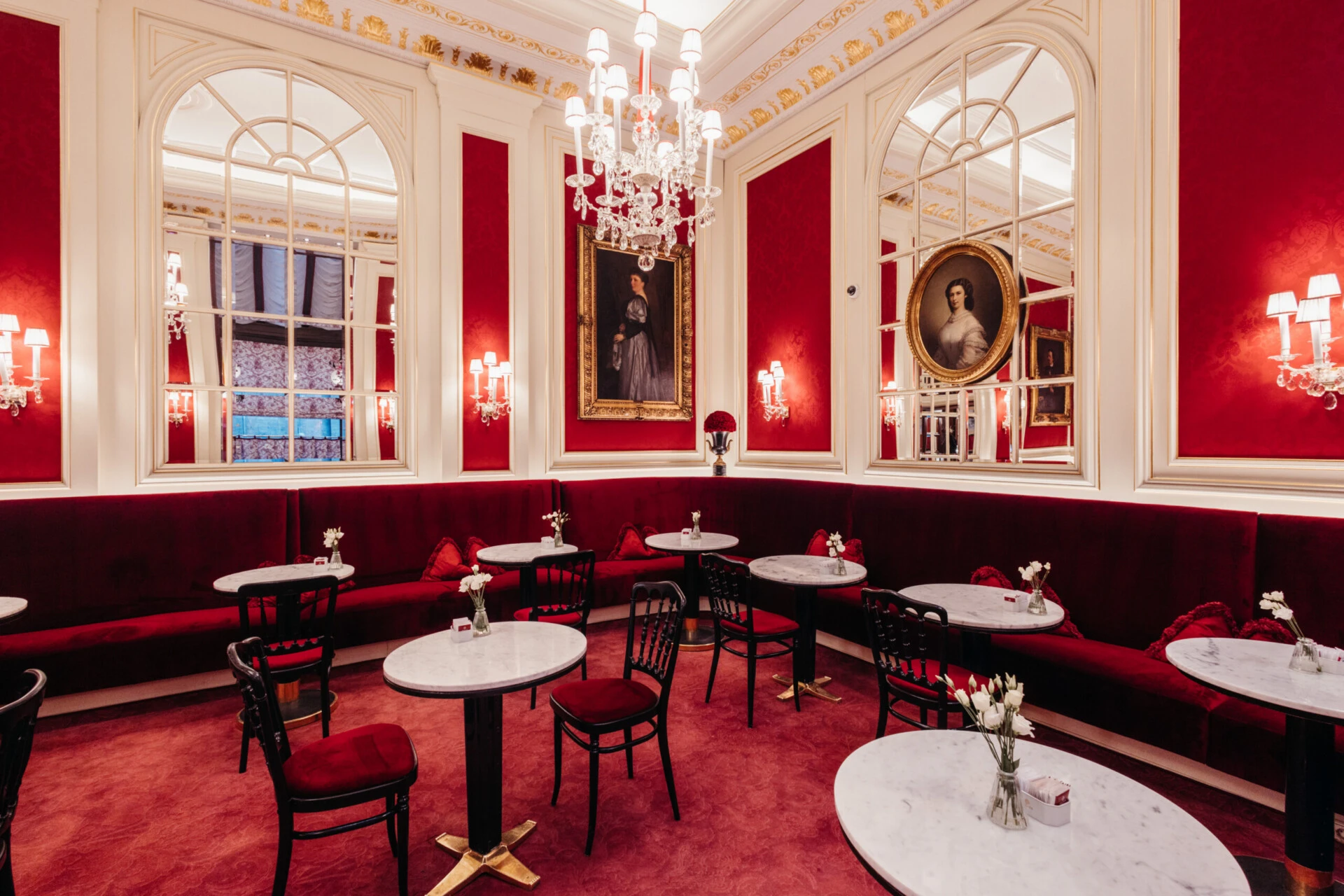 Elegant seating area at Café Sacher Vienna with red velvet benches, marble tables and a crystal chandelier.