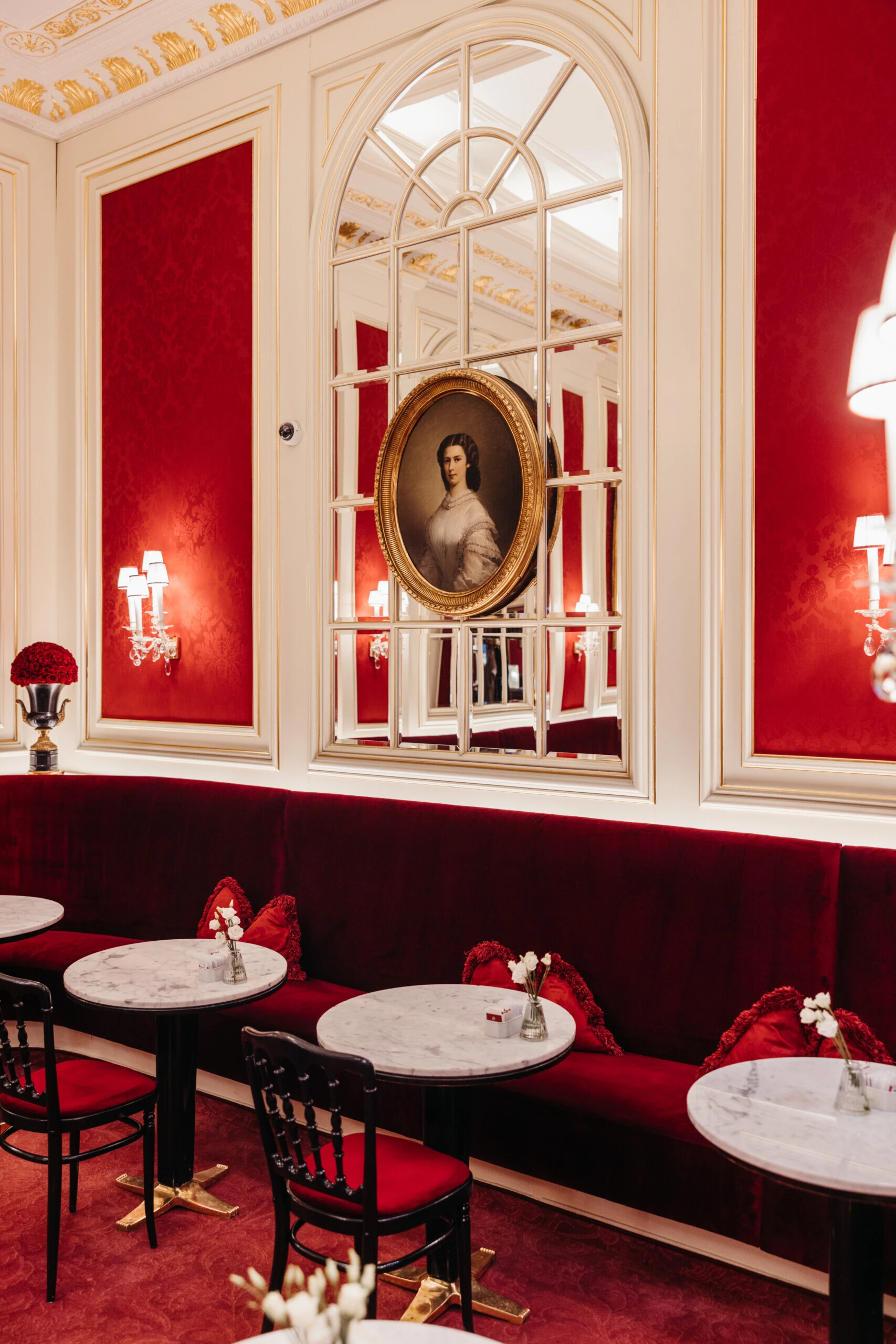 Interior detail of Café Sacher Vienna with a red velvet bench, portrait and wall mirrors.
