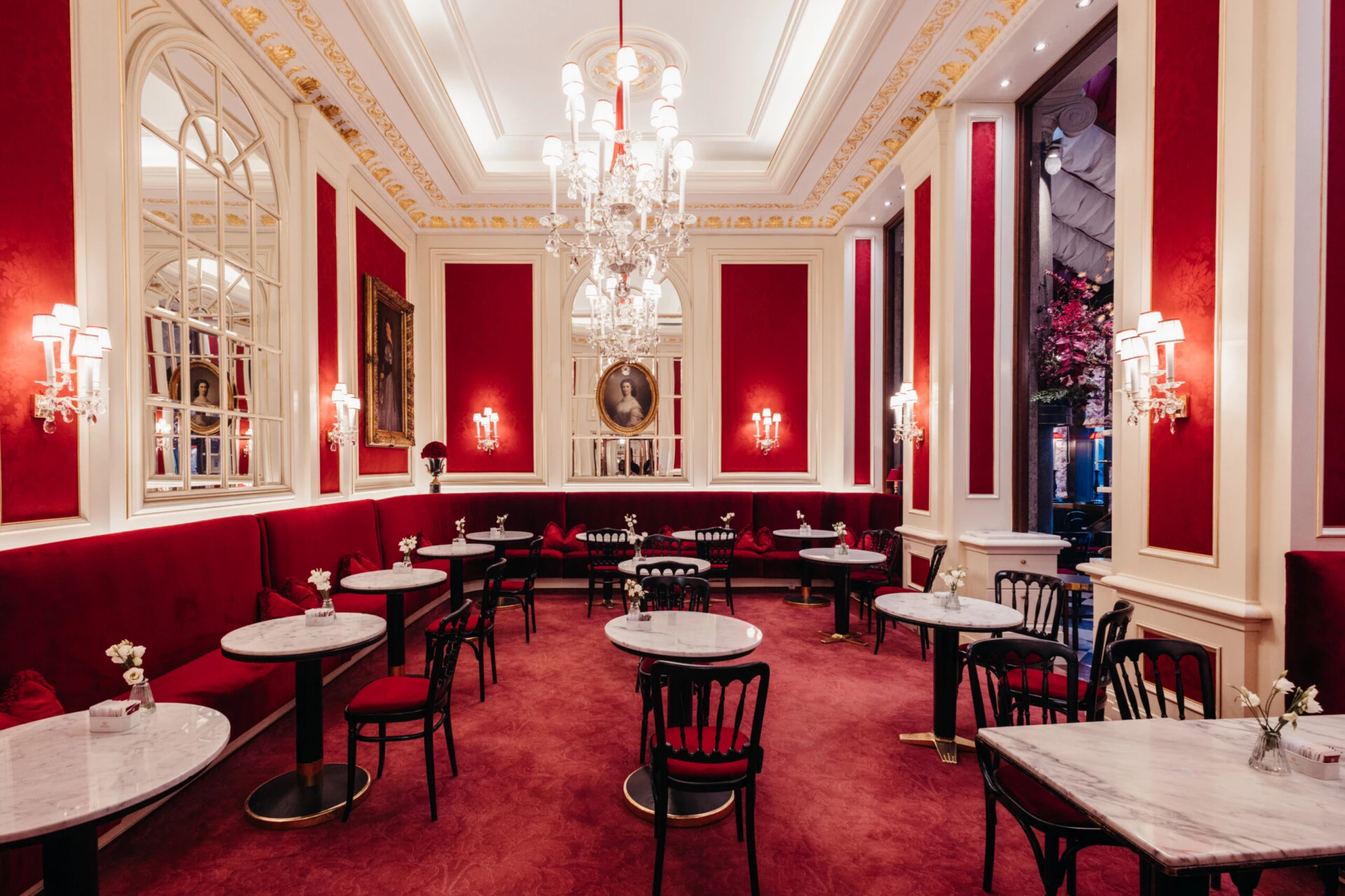 Bright dining room at Café Sacher Vienna with red velvet seating, marble tables and classic décor.