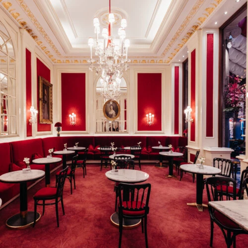 Bright dining room at Café Sacher Vienna with red velvet seating, marble tables and classic décor.
