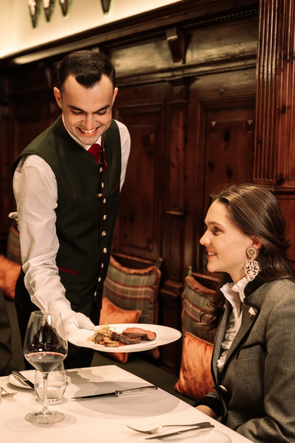 A staff member serves a dish to a guest in the fine dining restaurant Zirbelzimmer.